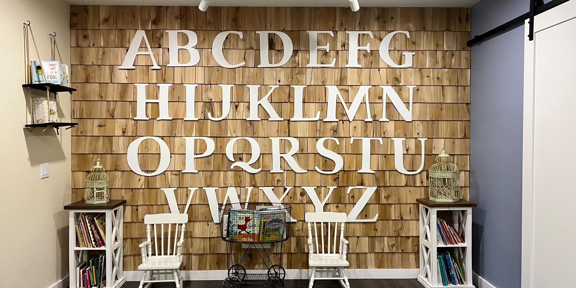 Wall of white letters on cedar shingles with child-sized furniture in front of it at Book Nook West End